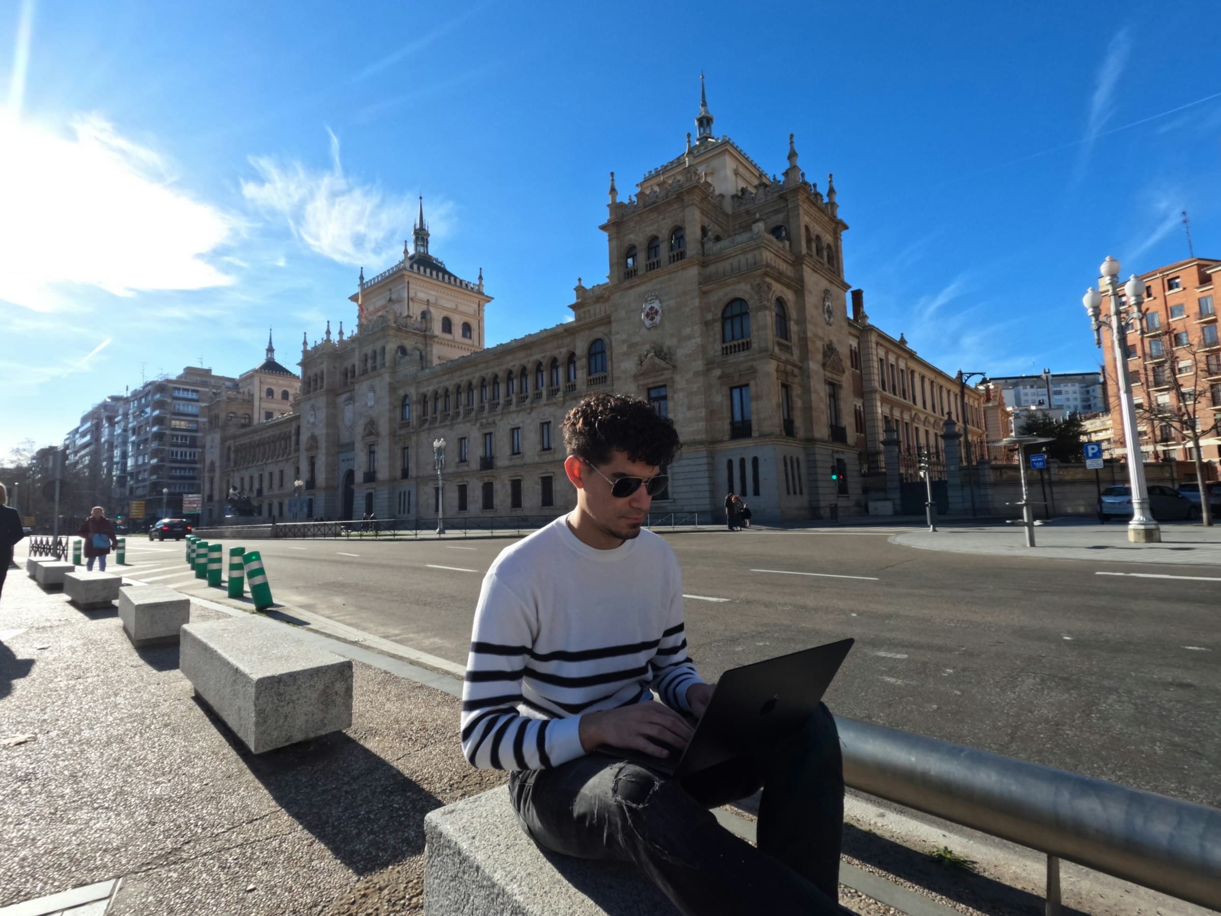 A man working on a laptop on a stone bench in a Spanish city square